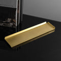 A long, rectangle shaped brass tray with raised edges upon a black reflective surface. The background wall is white and to the left of the tray is the coffee table book This Is Home: The Art of Simple Living. The brass tray is made by Empire Copper.