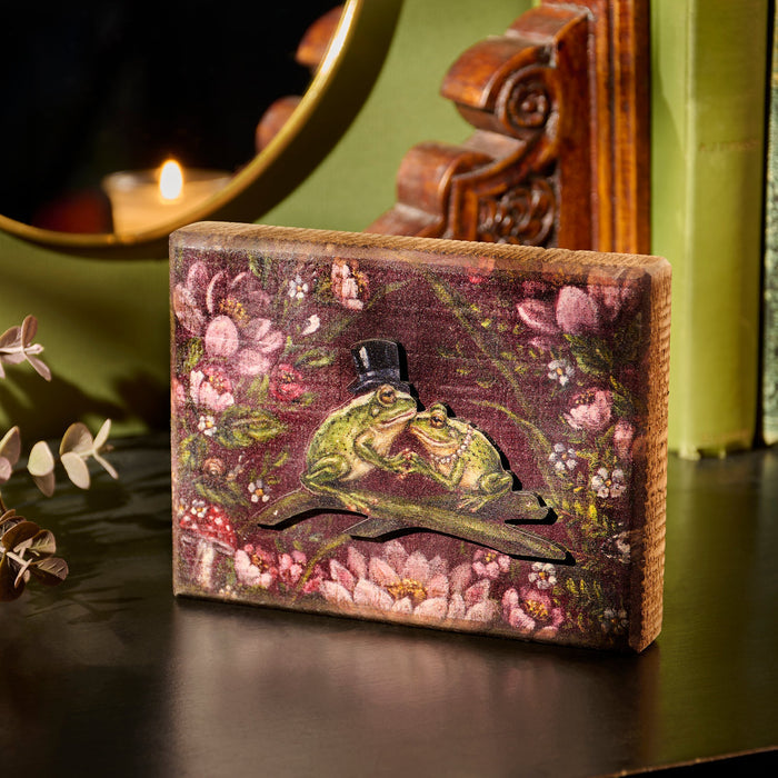 Decorative box with a frog design on a floral background, placed on a reflective surface.