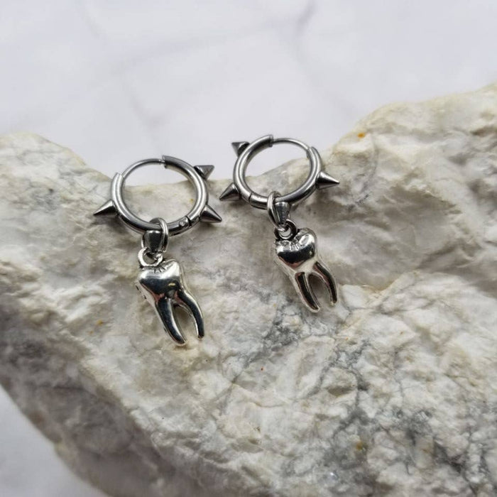 Pair of silver hoop earrings with tooth charms on a stone surface