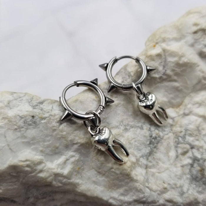 Pair of silver hoop earrings with spike details on a stone surface