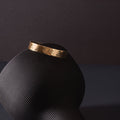 A planished brass cuff, twinkling in the light. The cuff is placed upon a black, turned over vase. The vase is upon a dark navy tabletop and the background is charcoal in colour. The brass cuff bracelet is made by Empire Copper.