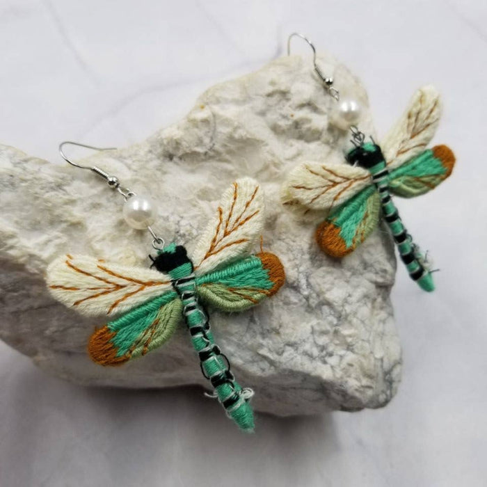 Dragonfly-shaped earrings on a rock with a white background