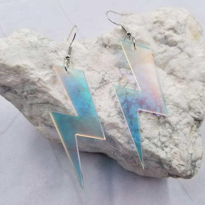 Iridescent lightning bolt earrings on a textured stone surface
