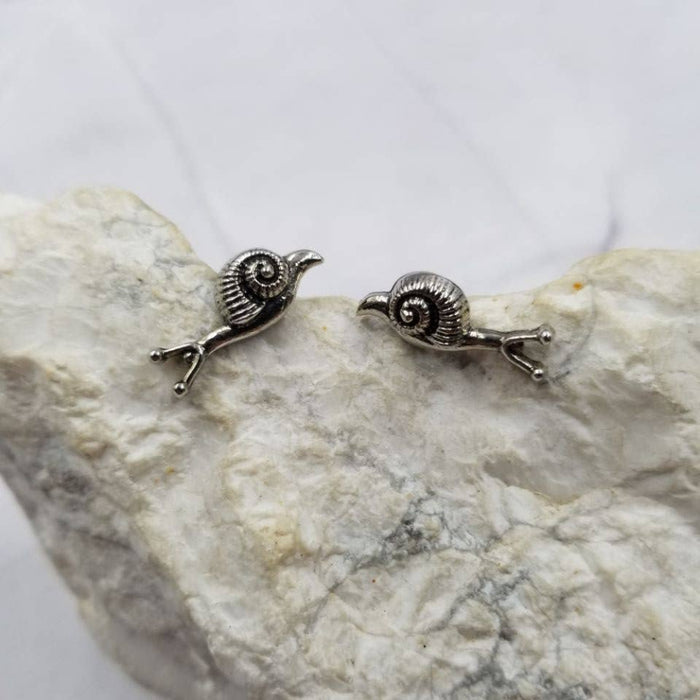 Pair of silver snail-shaped earrings on a stone surface