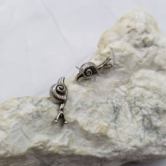 Pair of silver snail-shaped earrings on a textured stone surface