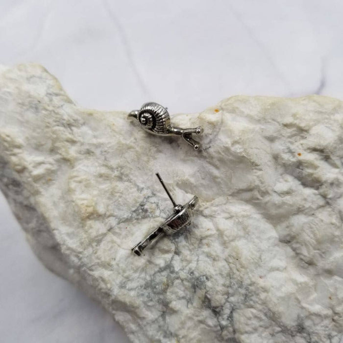 Silver snail-shaped earrings on a textured stone surface