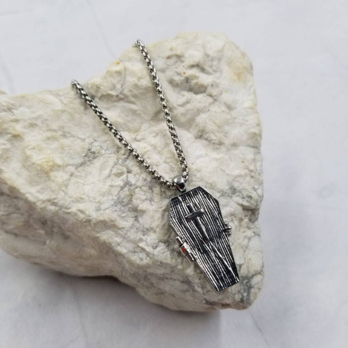 Silver necklace with a coffin pendant on a textured stone surface