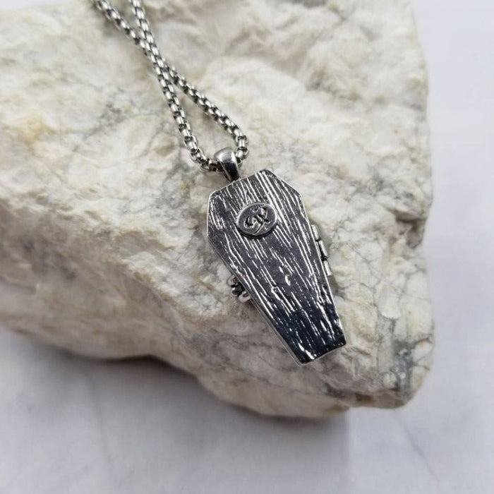 Silver coffin-shaped pendant on a chain against a stone background